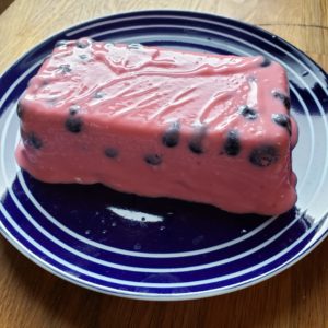 Pink molded jello on a blue plate with blueberries