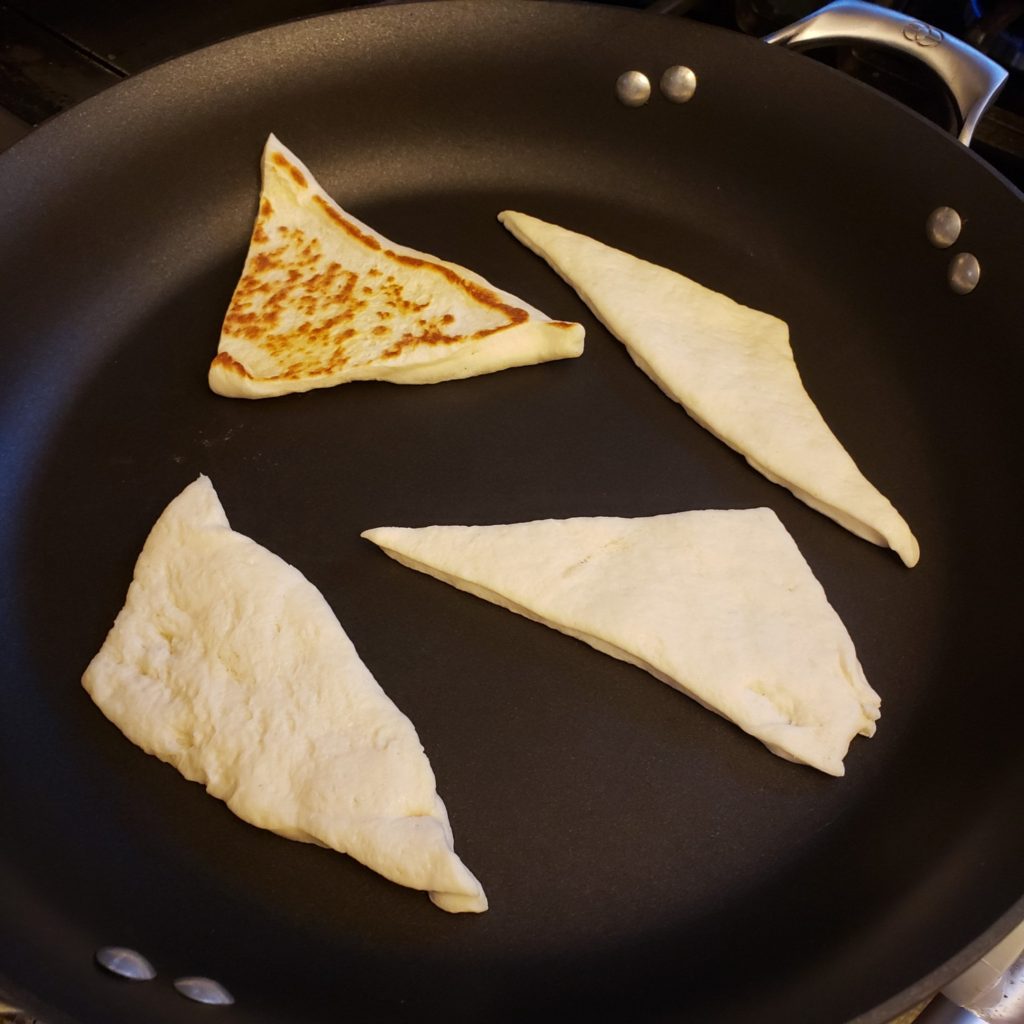 Pillsbury Pizza Dough cut into triangles and cooking in a black skillet