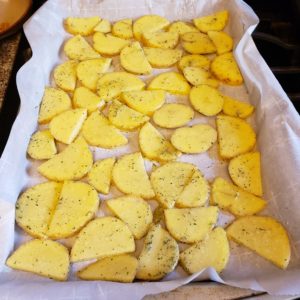 Seasoned potatoes spread over a baking sheet lined with parchment paper