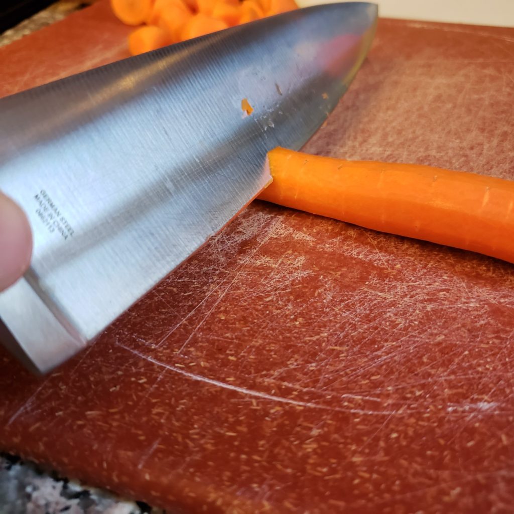 Carrot being cut on a red cutting board with a chefs knife