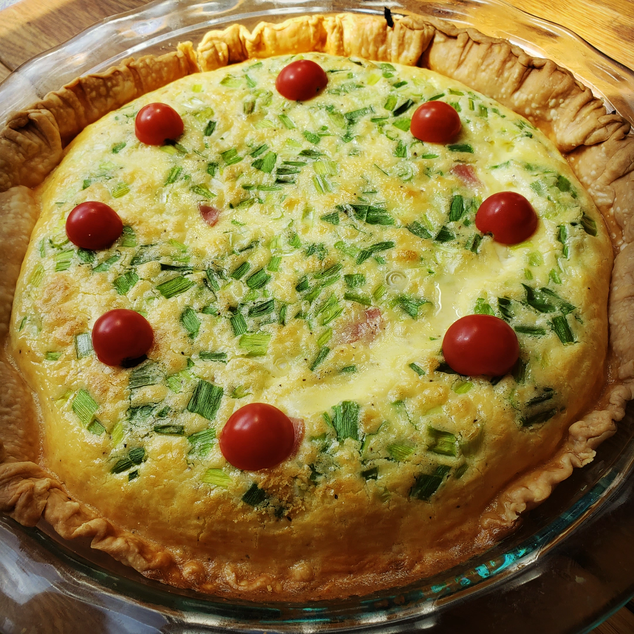 quiche in a pie pan, with green onions and cheery tomatoes on top